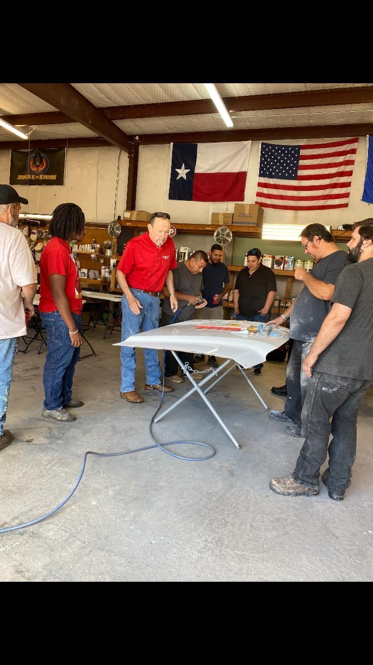 People gathered around a table inside a workshop, Texas and US flags in the background.
