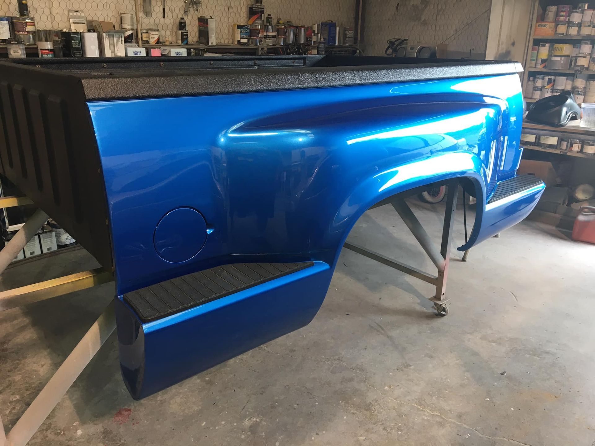 Blue truck bed with black bed liner, in a shop.