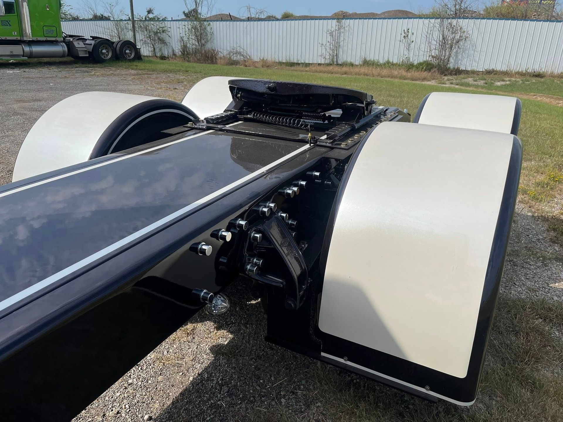 Black truck chassis with white fenders, outdoors.