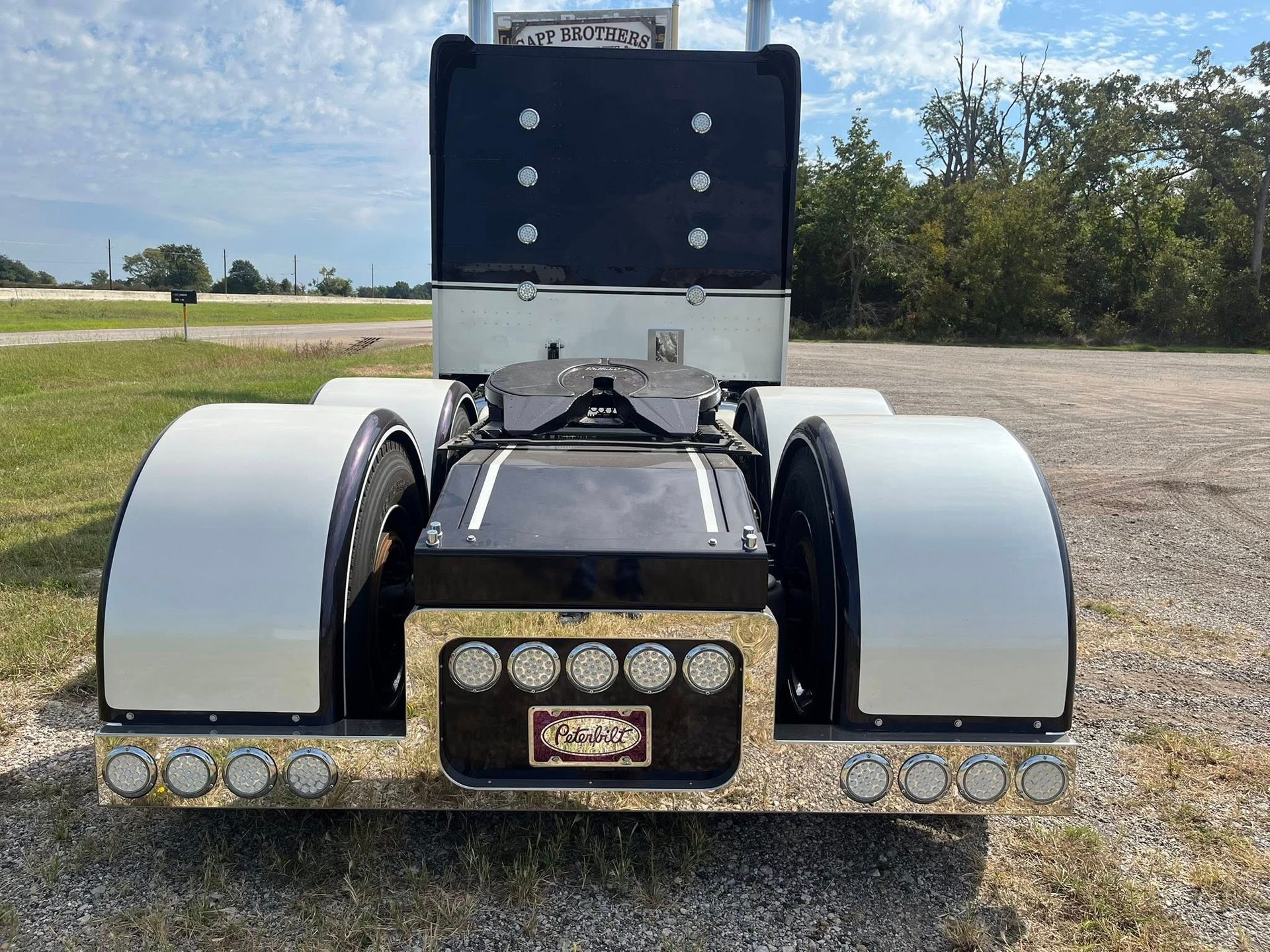 Rear view of a black and chrome semi-truck. White fenders, black frame, chrome lights. Outdoors.