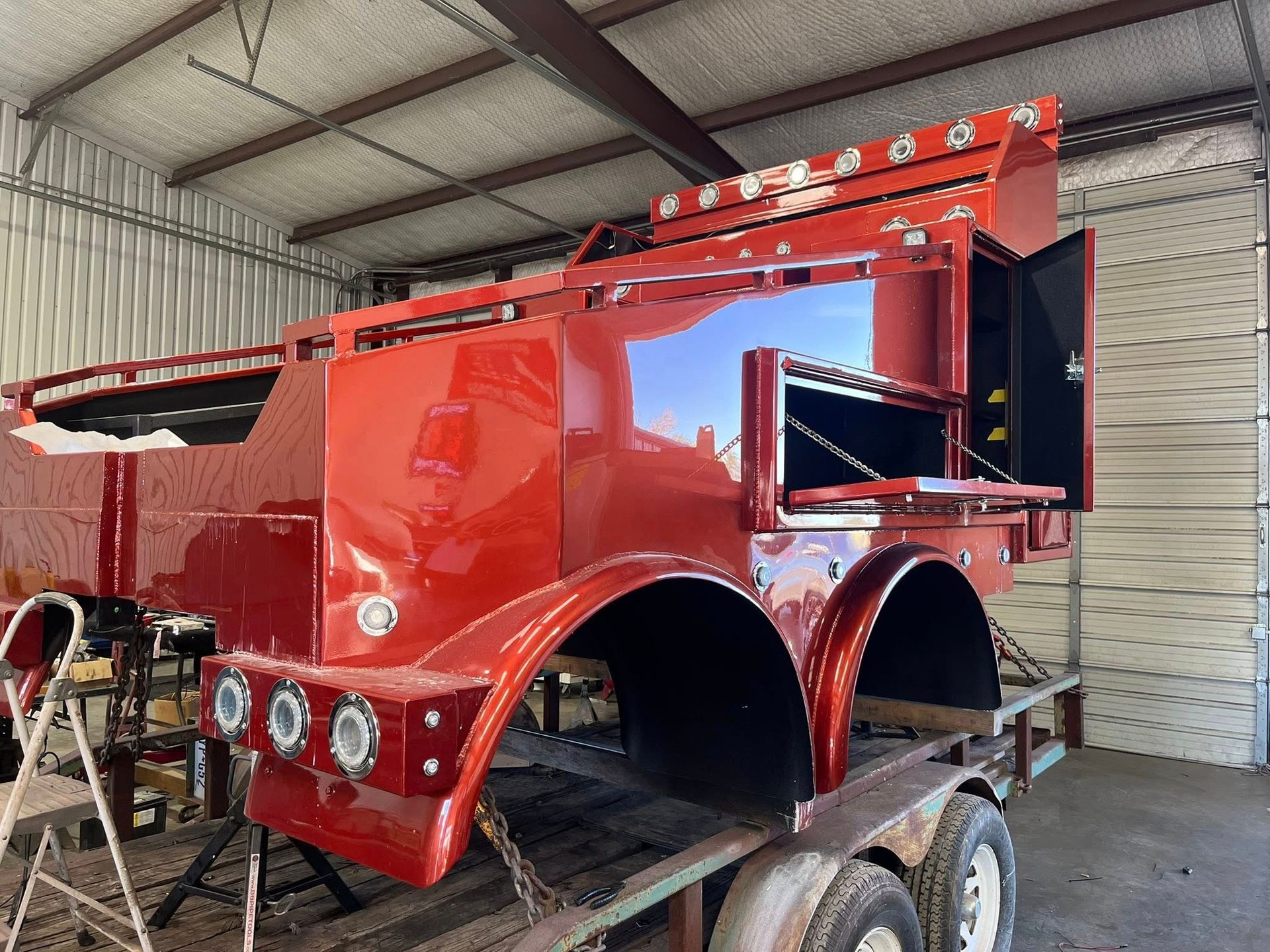 Red custom truck bed with toolboxes and storage, mounted on a trailer inside a workshop.