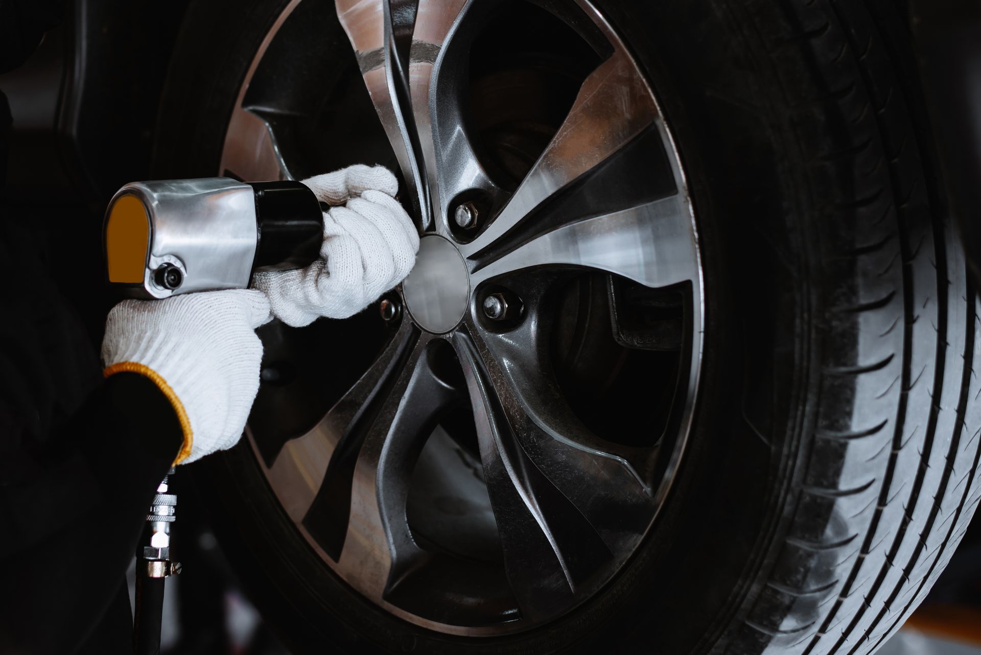 A hand tightening the bolts when putting on a new tyre. The user is wearing white gloves with an orange trim.