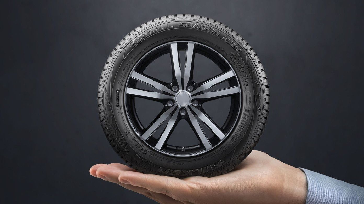 A man's hand holding a clean new tyre in his palm. The background is black.