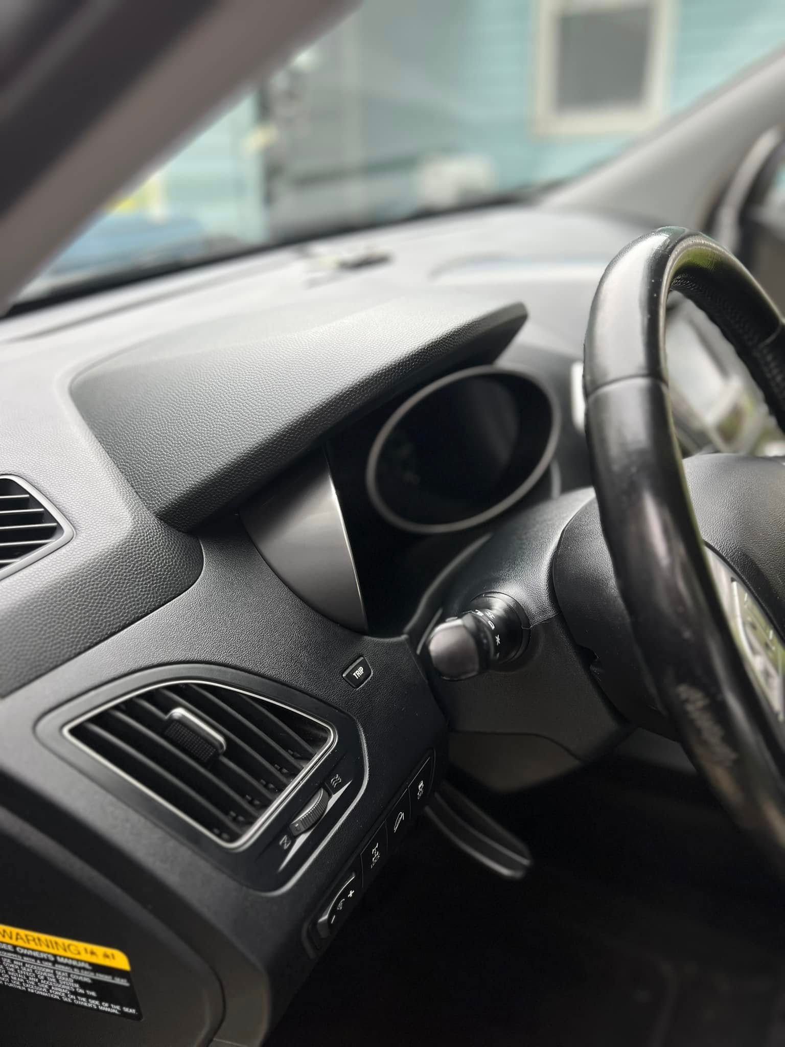 Interior view of a vehicle's driver-side dashboard, showing the steering wheel, instrument cluster, and air vent.