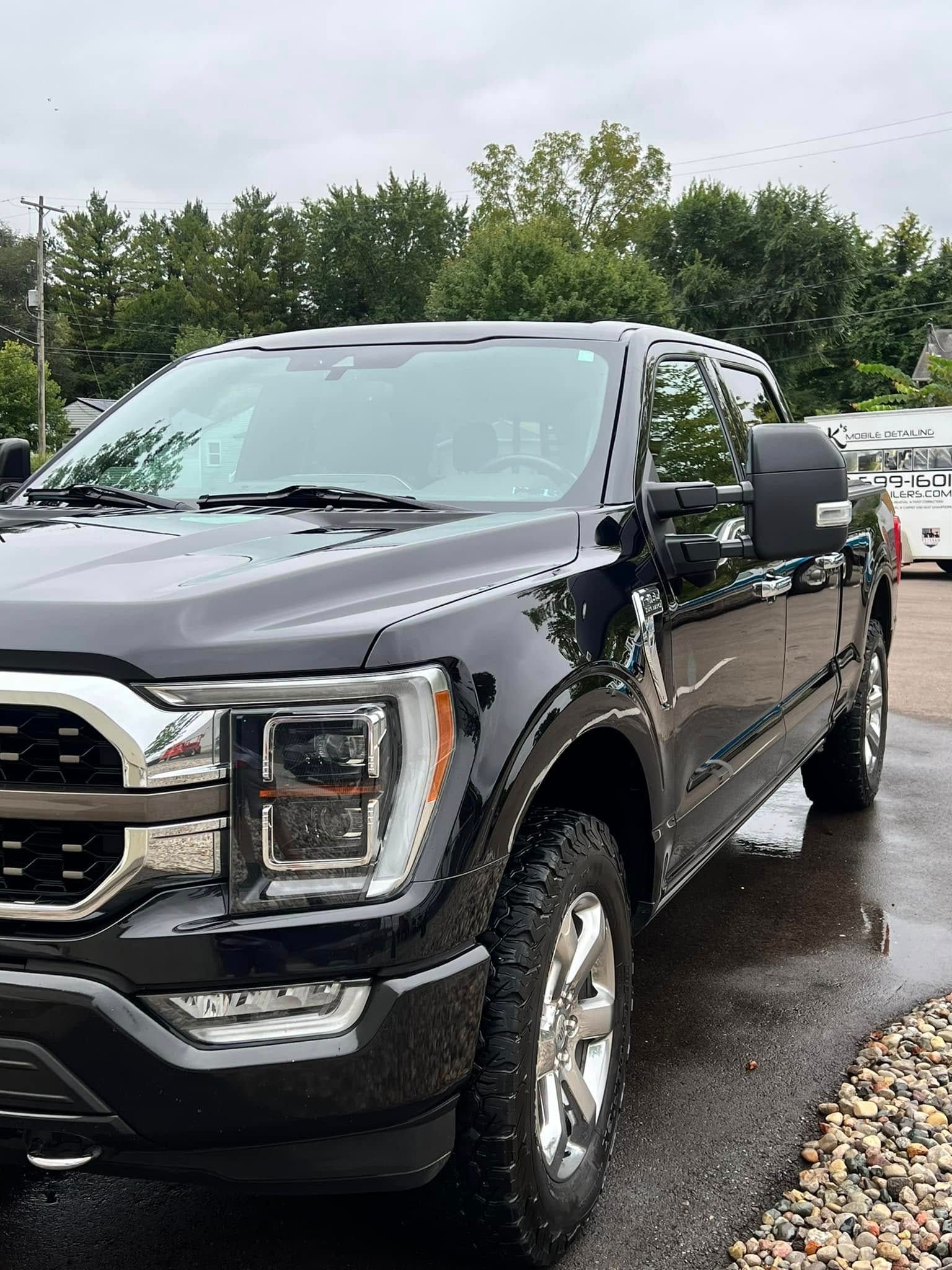 A black Ford F-150 pickup truck parked outdoors on a cloudy day, showcasing its front grill, headlights, and side profile.