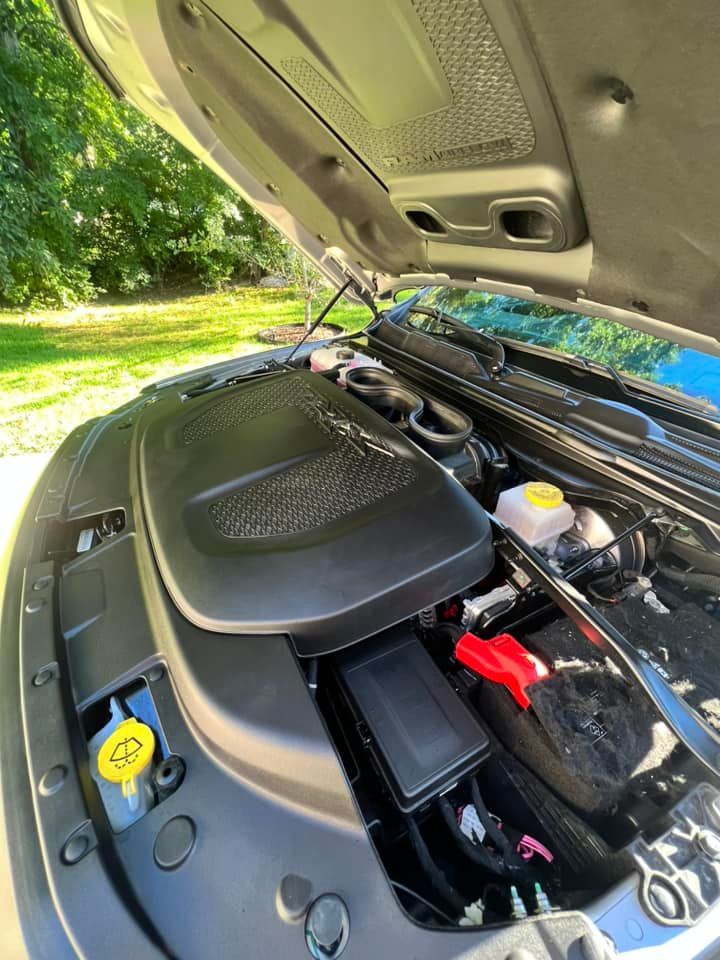 The open hood of a vehicle showing the engine compartment, including the engine cover, fluid reservoirs, and battery.