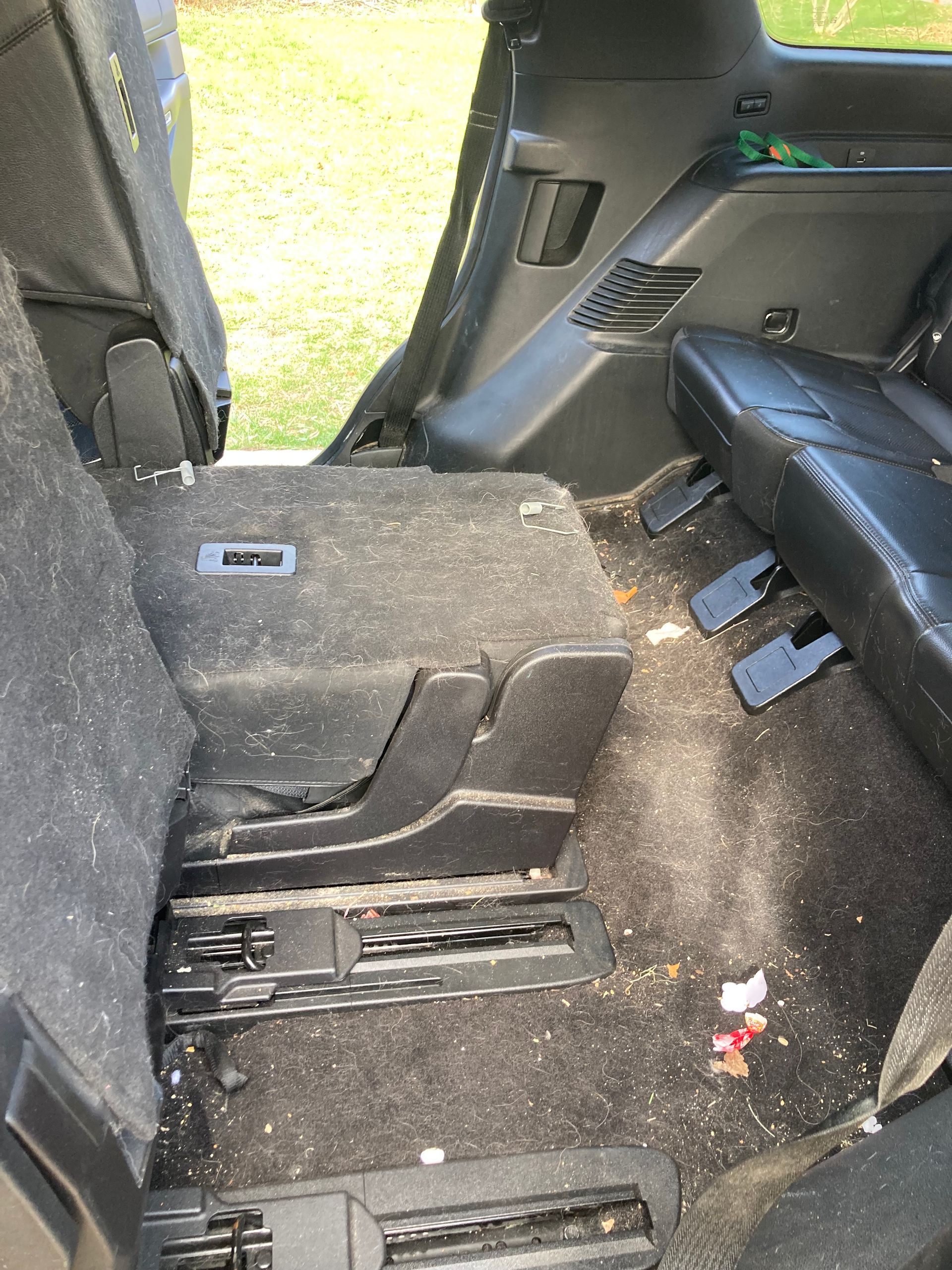 An interior view of a vehicle showing folded rear seating, black upholstery, and debris on the dark carpeted floor.