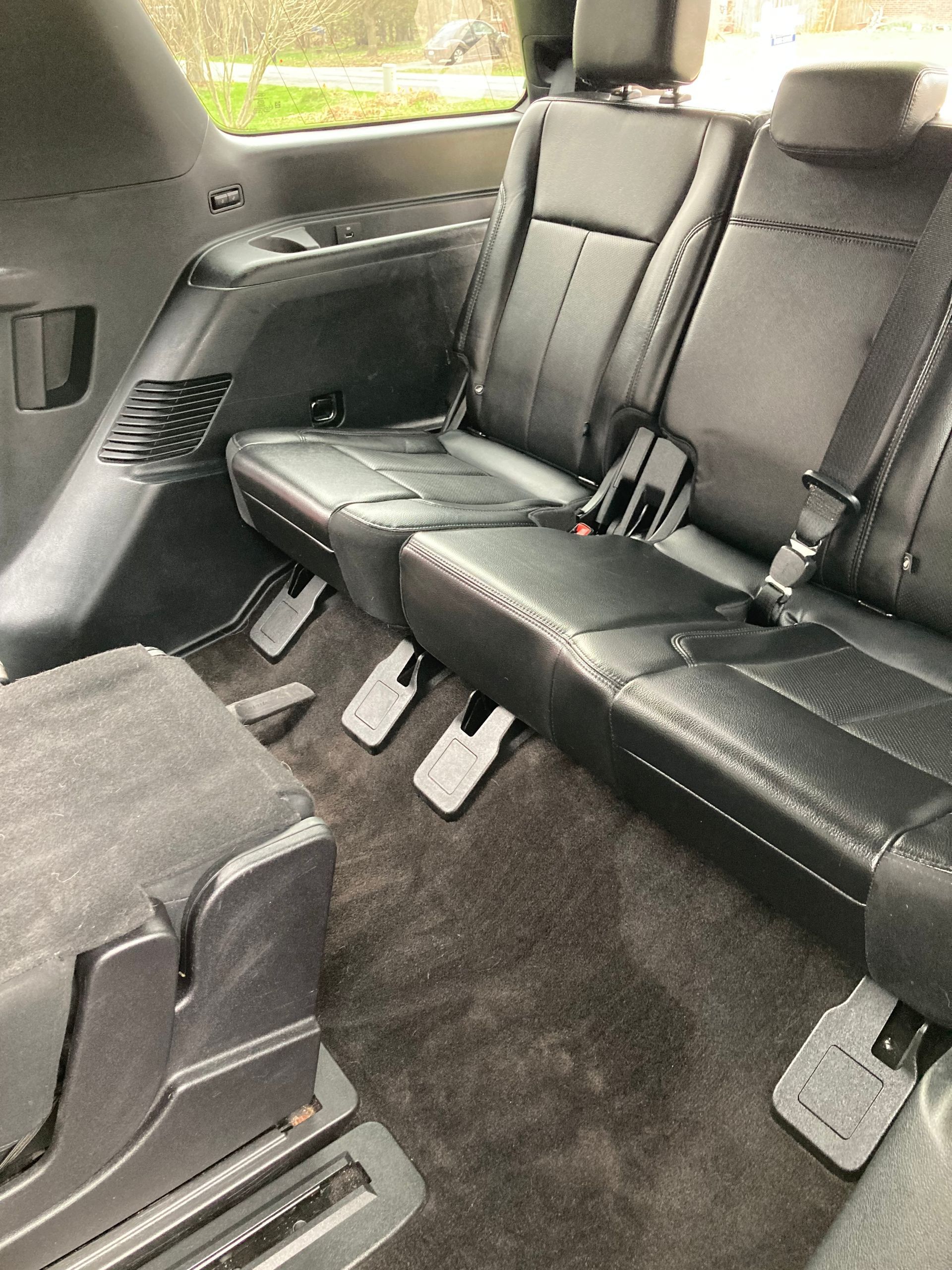 A view inside a vehicle showing black leather second-row seats and a folded third-row seat on black carpet.