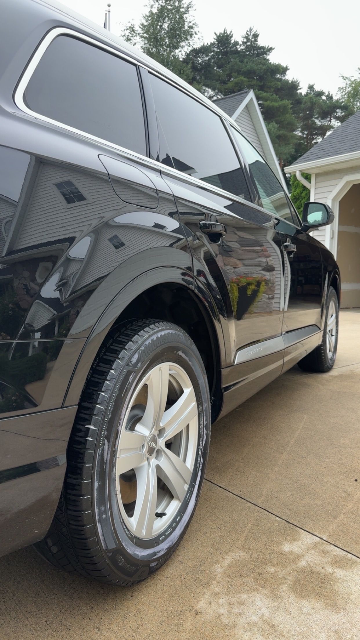 Black SUV parked in a driveway, side view with wet pavement and trees in the background
