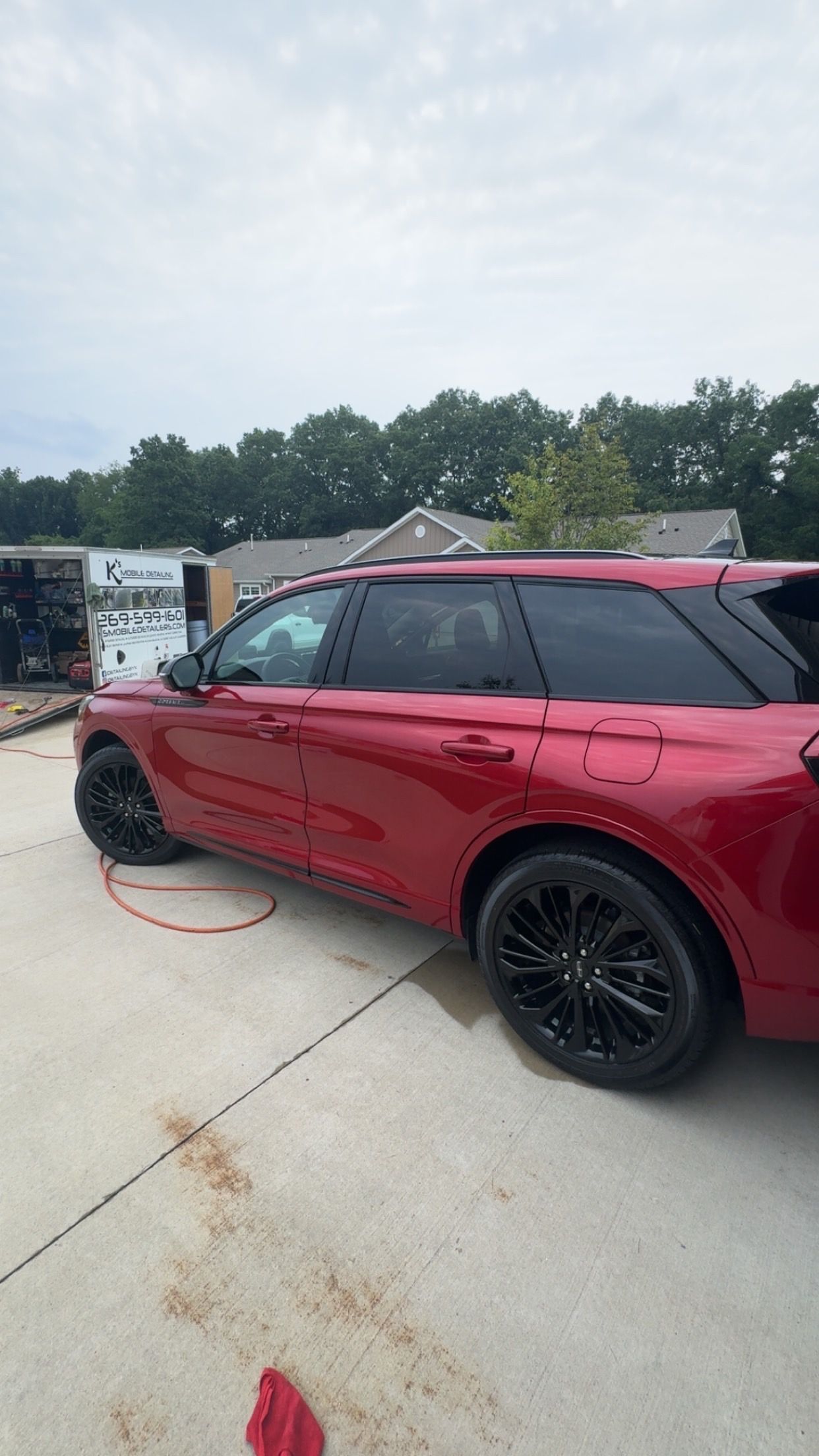 Red SUV parked on a driveway beside a white boat trailer, with trees in the background.