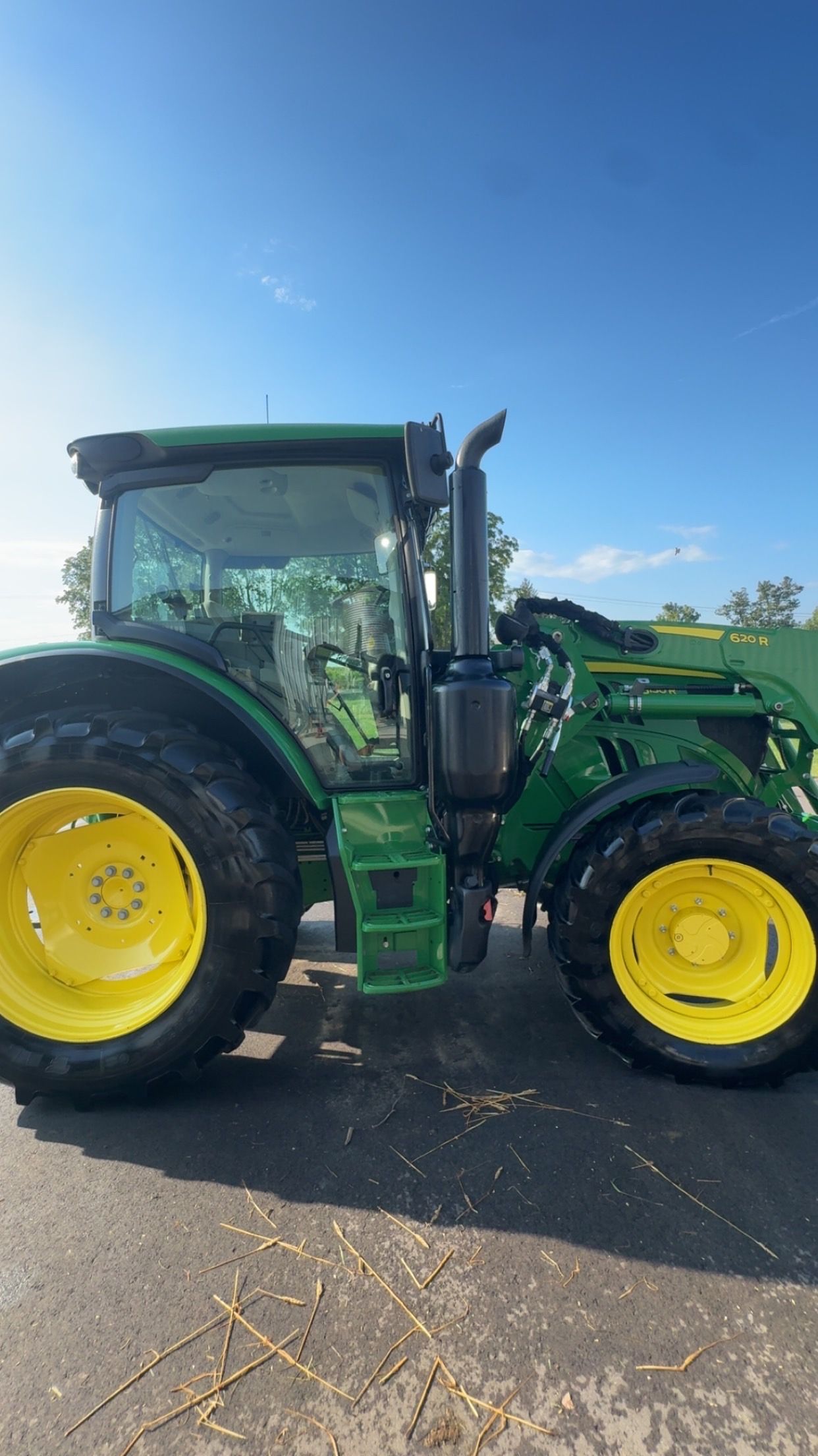 Green tractor with yellow wheels parked on a gravel surface under a clear blue sky