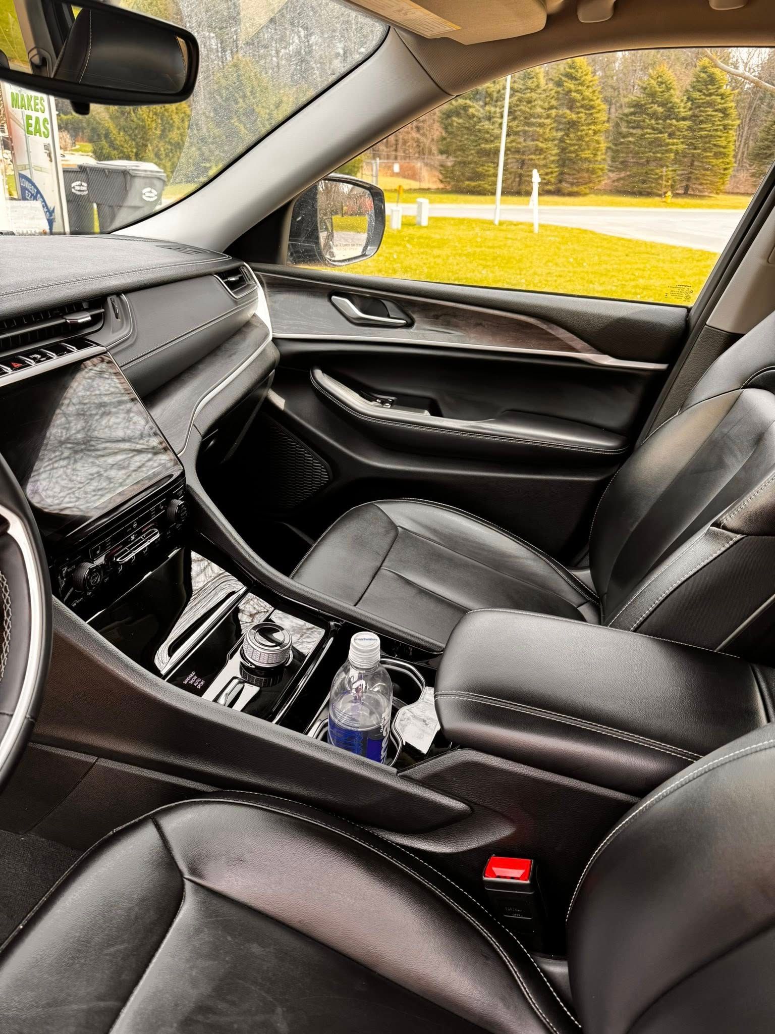 Interior view of a black leather car cabin with a bottle in the center console and a window view of trees and grass.