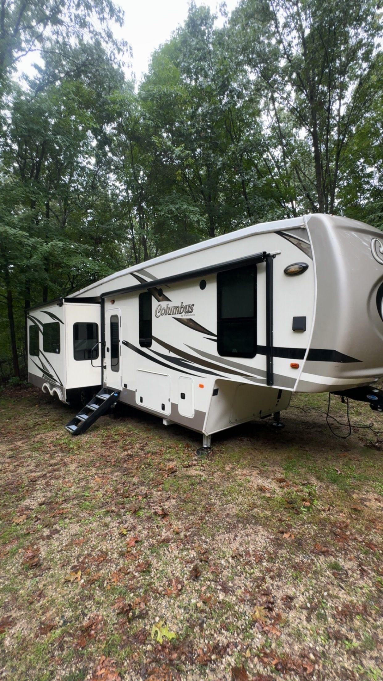 White and gray Jayco travel trailer parked outdoors beside a propane tank on a sunny day