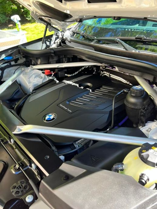 Engine bay of a BMW car with a black engine cover, prominent silver strut braces, and fluid reservoirs under the hood.