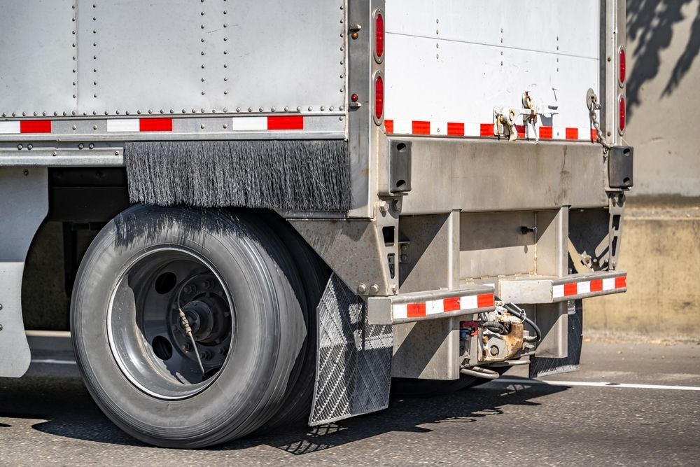 Close-up of a semi-truck’s rear wheel and undercarriage on a road.