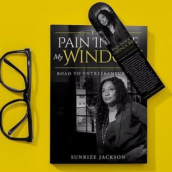 Black eyeglasses beside a book, Paint My Wind Road to Entrepreneur, with a matching bookmark on a yellow background
