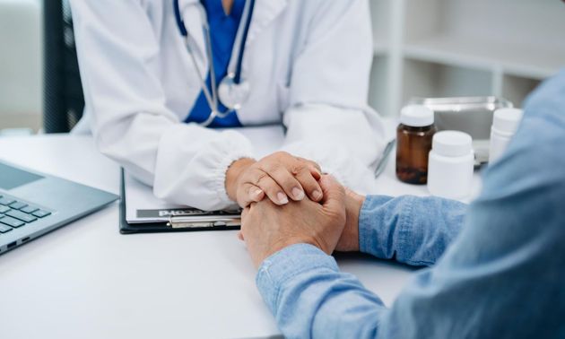Doctor holding a patient’s hands across a desk in a clinic office, conveying reassurance and support