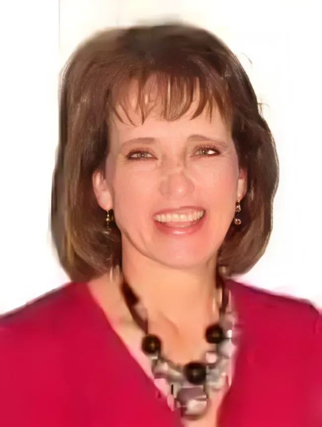 Smiling woman in a pink top and black necklace against a white background
