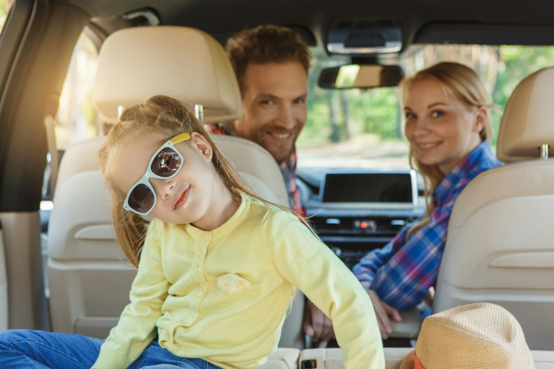 Happy family in a car, with a child in sunglasses smiling in the foreground.