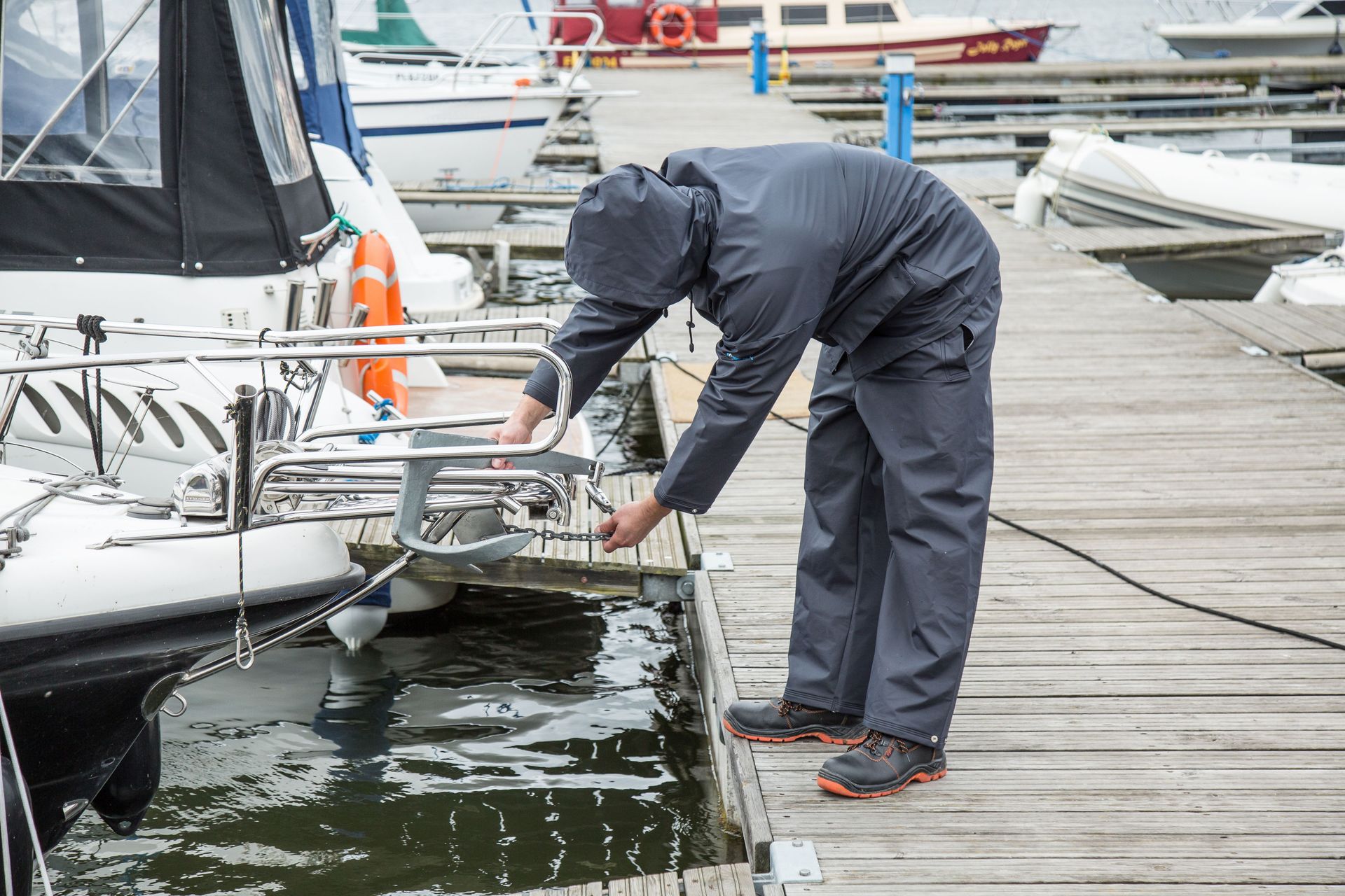 Person in dark rain gear adjusting a boat at a marina dock.