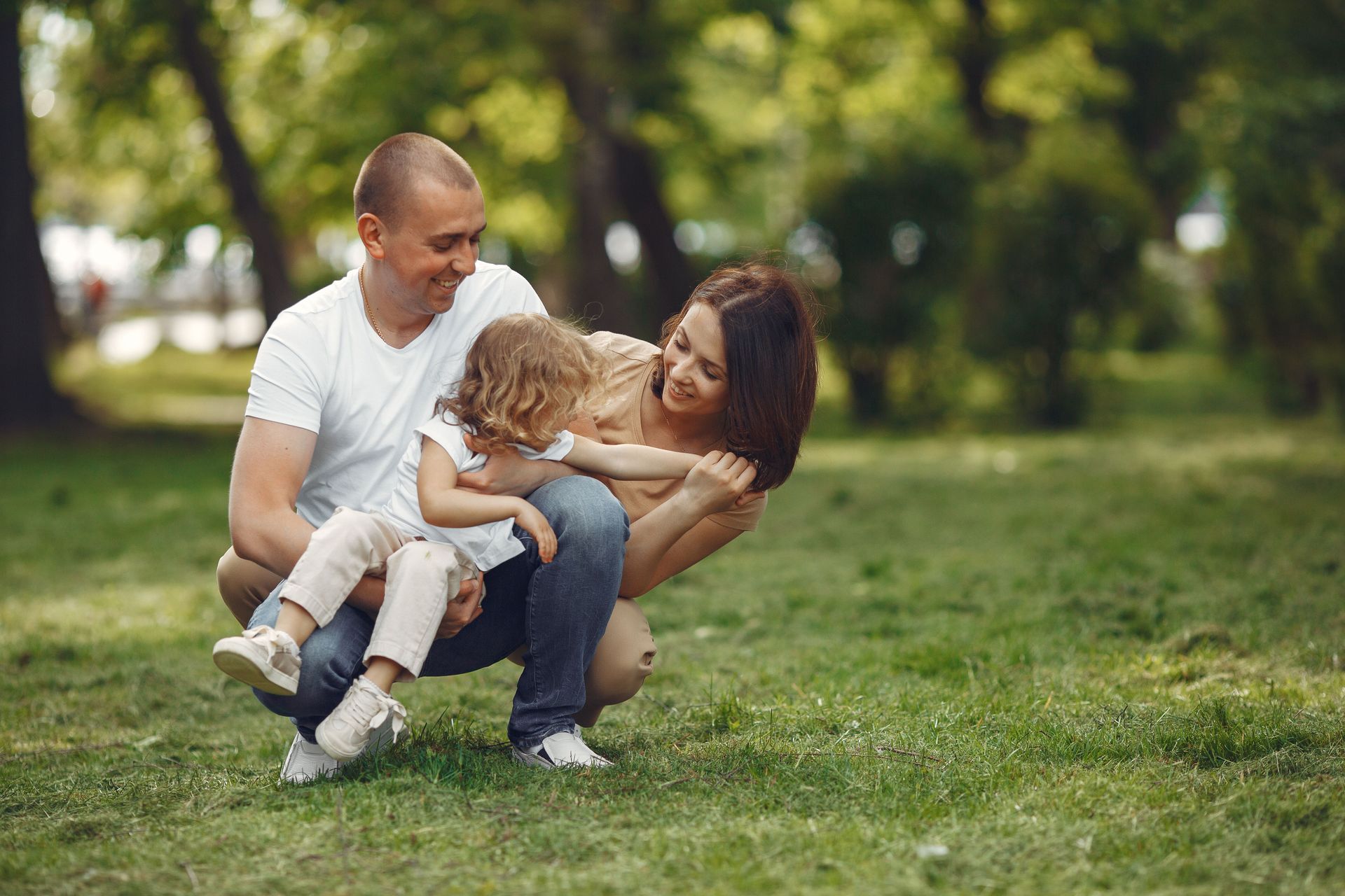 Two adults playing with a child on grass in a sunlit park