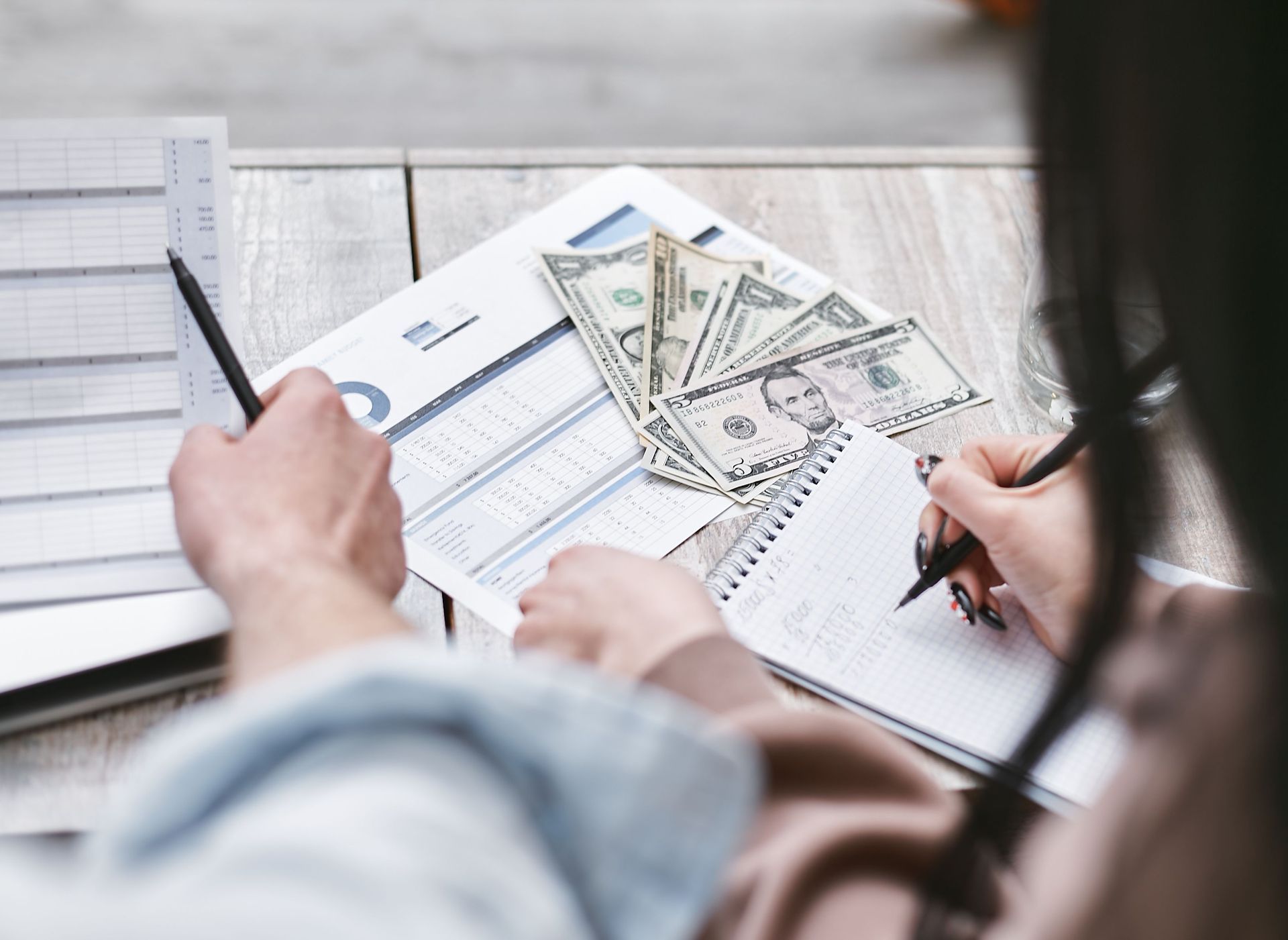 Hands reviewing financial documents with cash and a pen on a desk