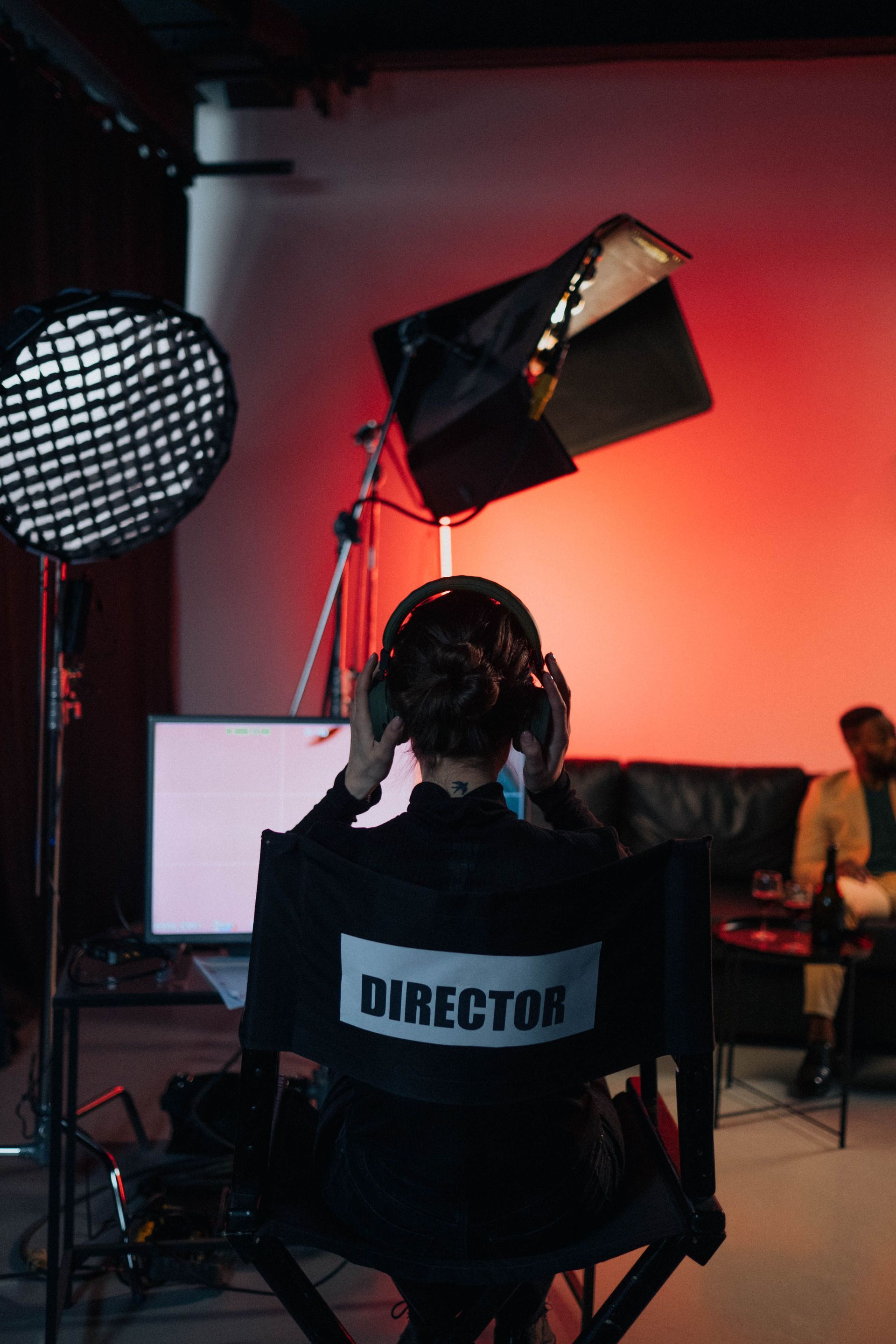 Director seated on set in a studio, facing lighting and a monitor under red lighting.