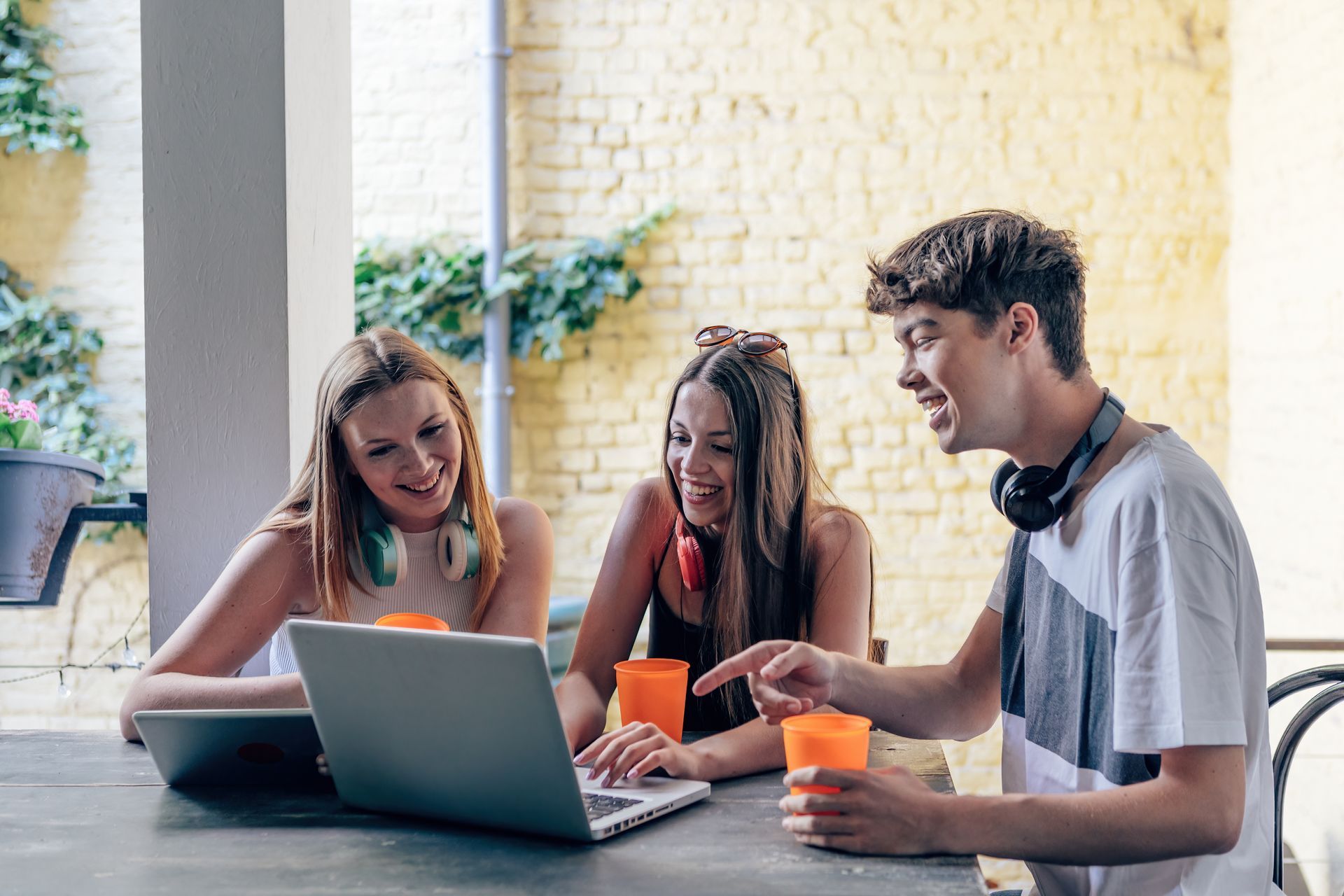 Three people collaborating around a laptop at an outdoor table, smiling and talking.