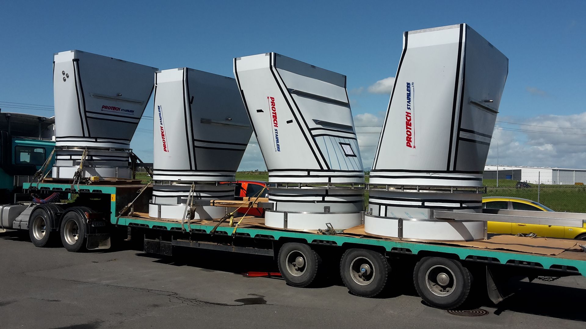 Four large, white industrial components secured on a flatbed truck for transport, with a clear sky backdrop.