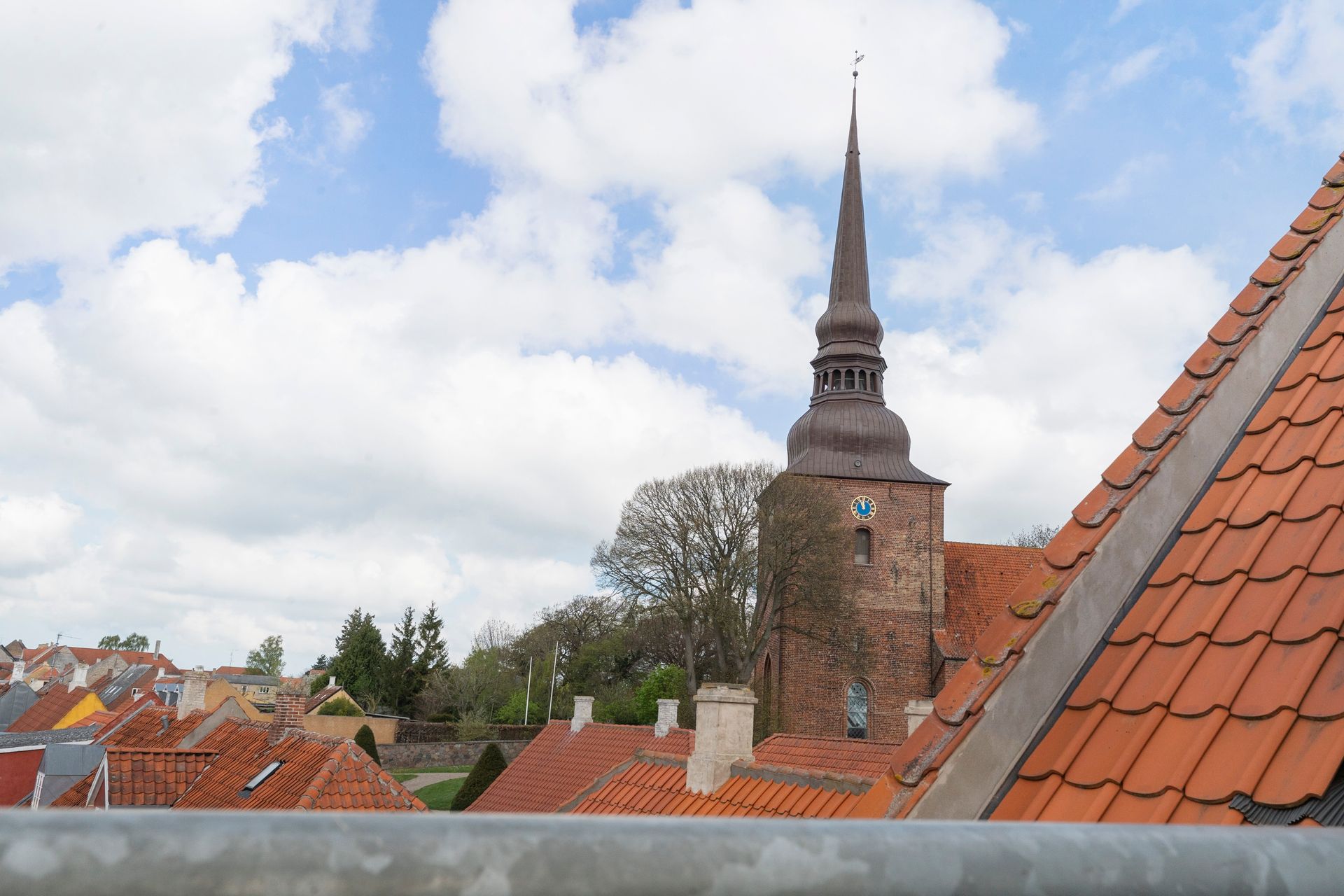 Kirketårn rejser sig over orange hustage under en overskyet himmel.