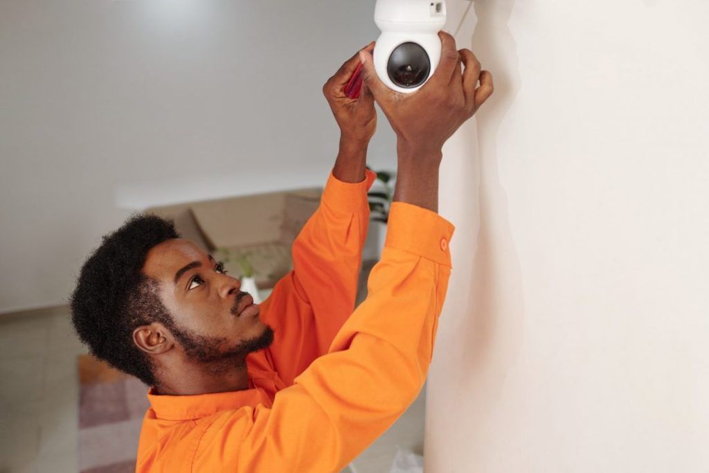 A man is installing a security camera on a wall.