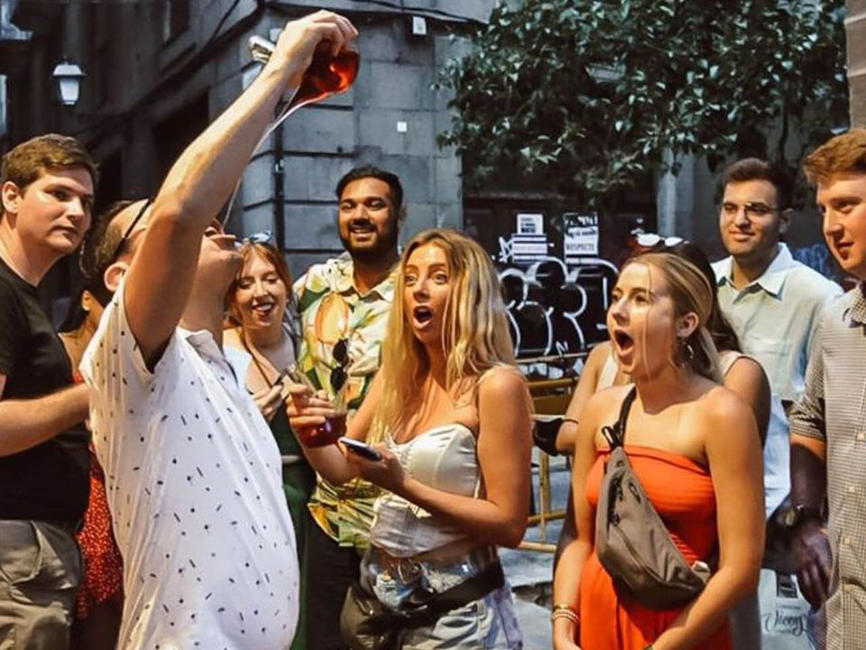 Tour guests in a Gothic Quarter street cheering as one drinks wine from a traditional porrón