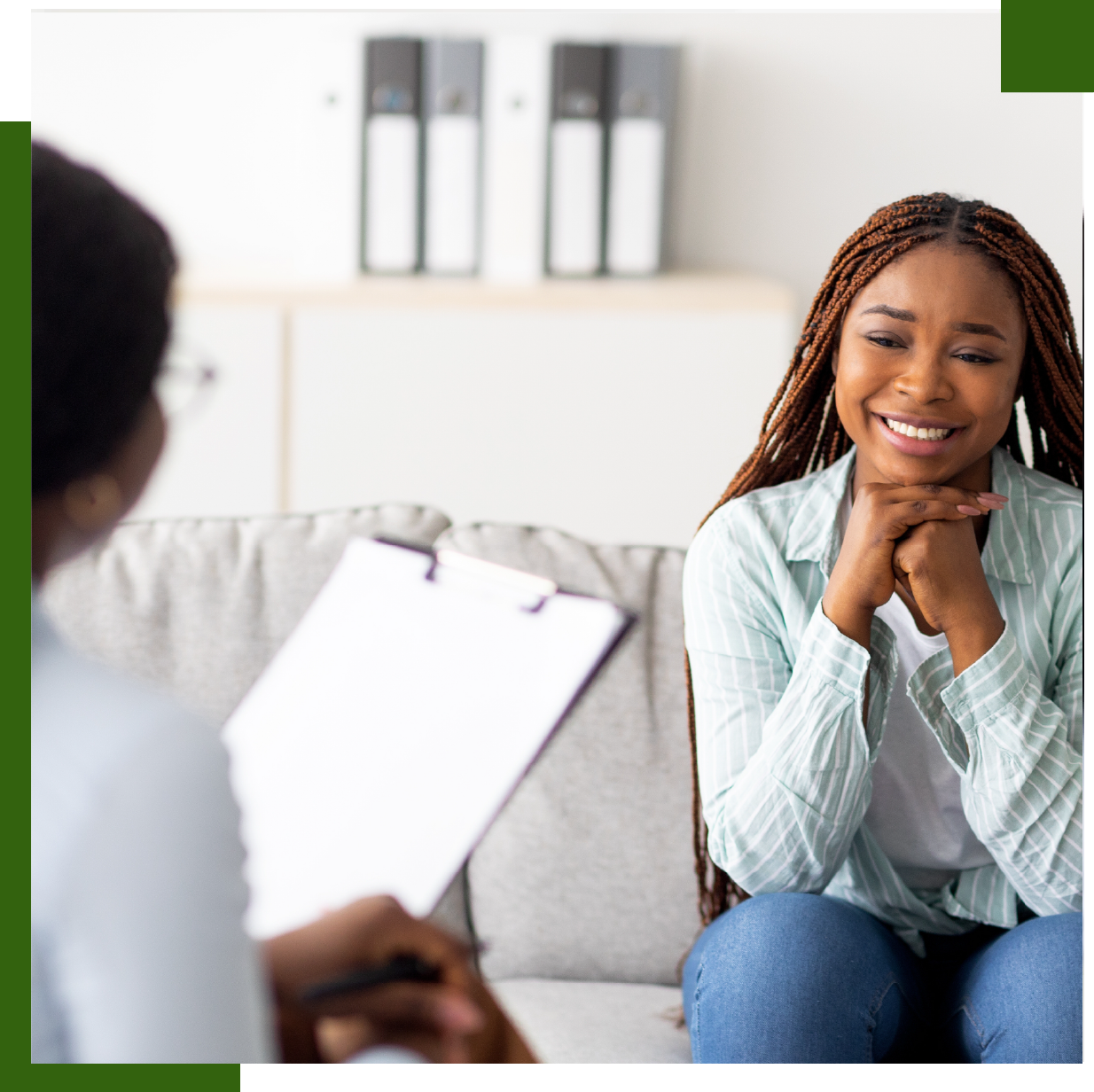 Woman smiling, hands clasped, sits on a couch in therapy session.
