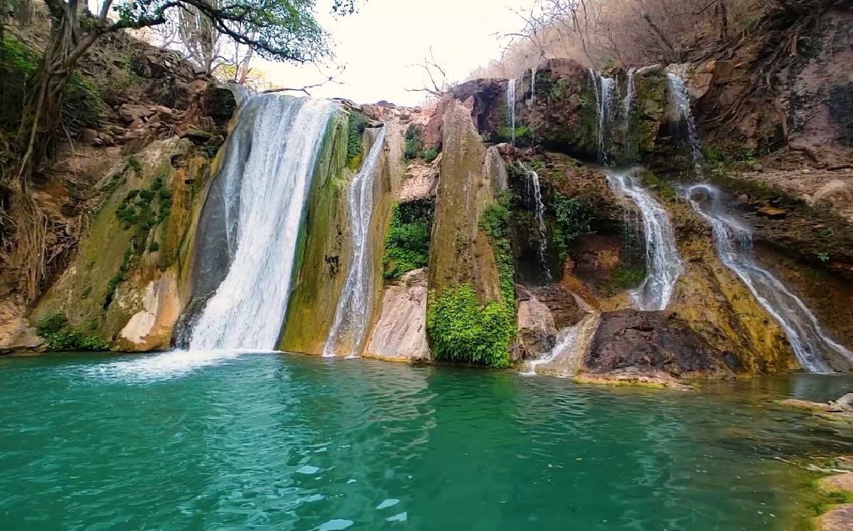 Cascada que cae en una poza de color turquesa en un cañón rocoso y exuberante.