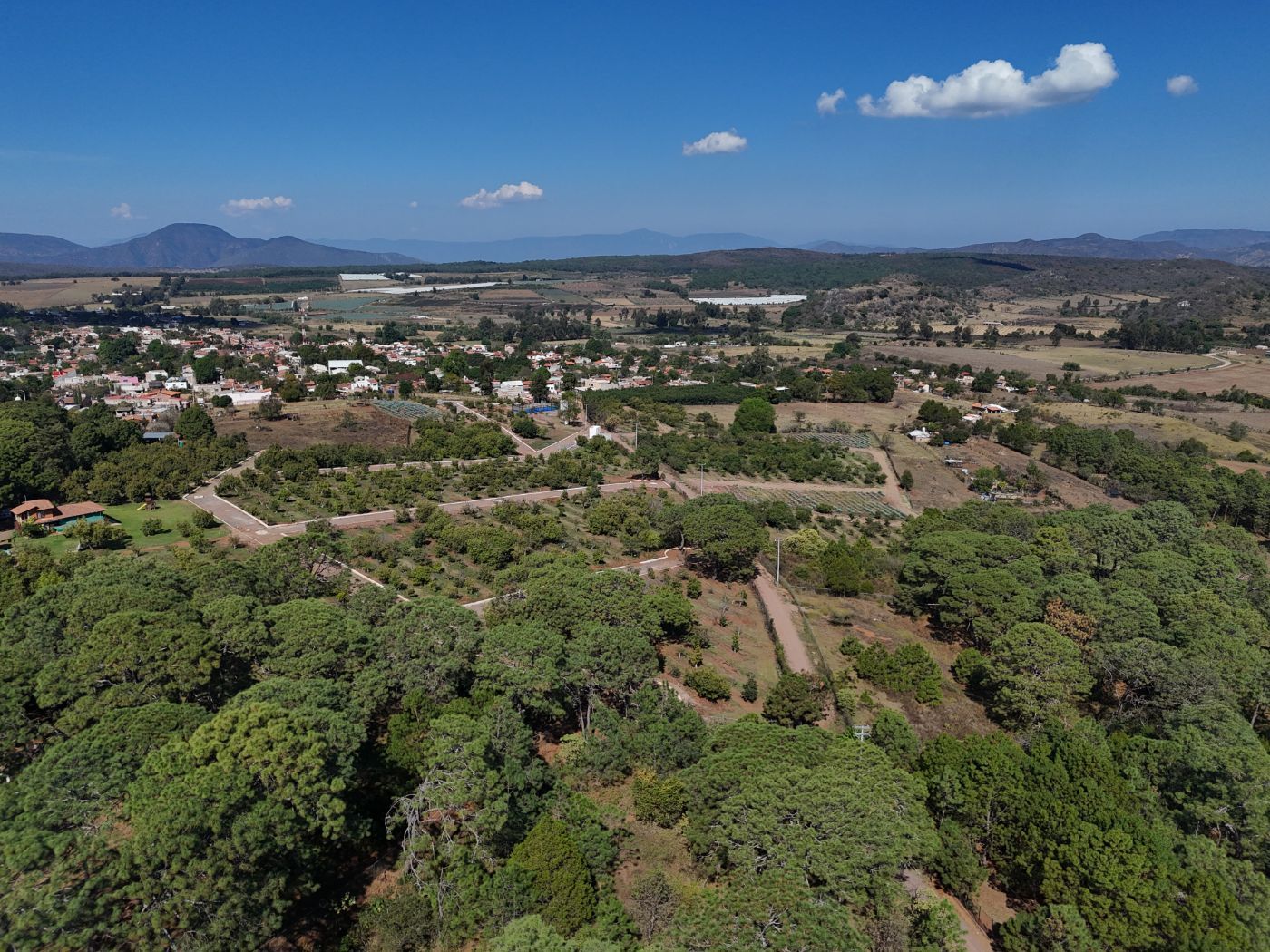 Vista panorámica de un valle verde y un pueblo con montañas bajo un cielo azul despejado.
