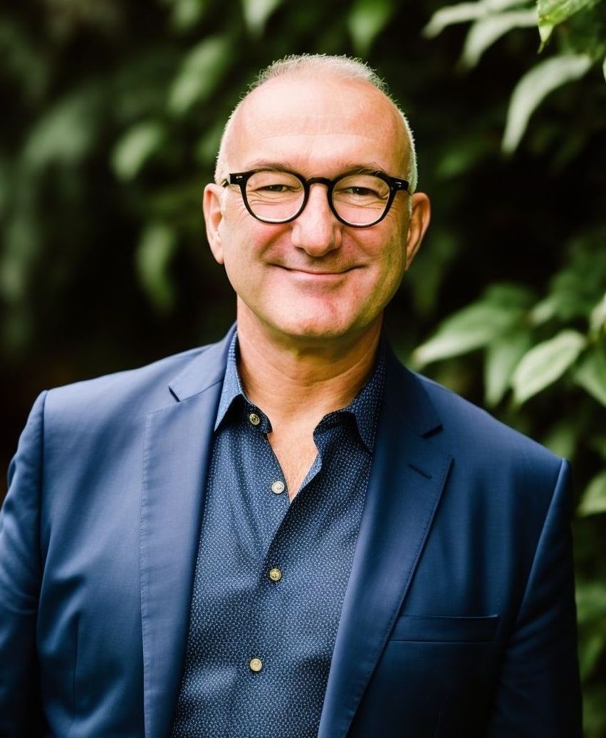 A man in a blue suit and glasses is smiling for the camera.