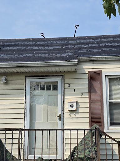 Front door of a beige house with black railing, brown shutters, and a slate roof under blue sky