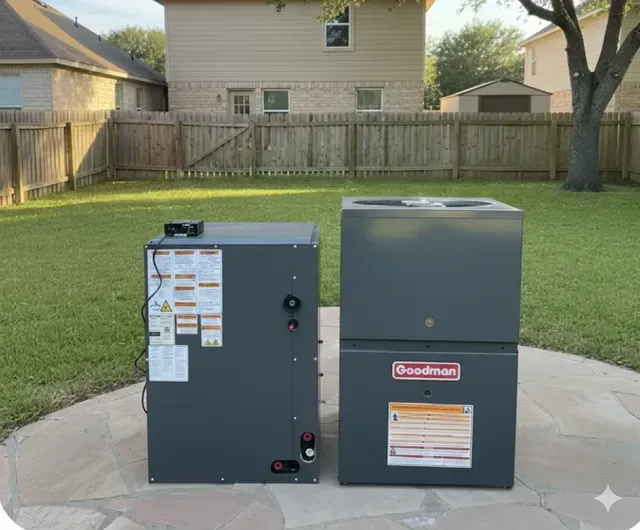 Two gray HVAC units sit outdoors on a stone patio, with a backyard and house in the background.