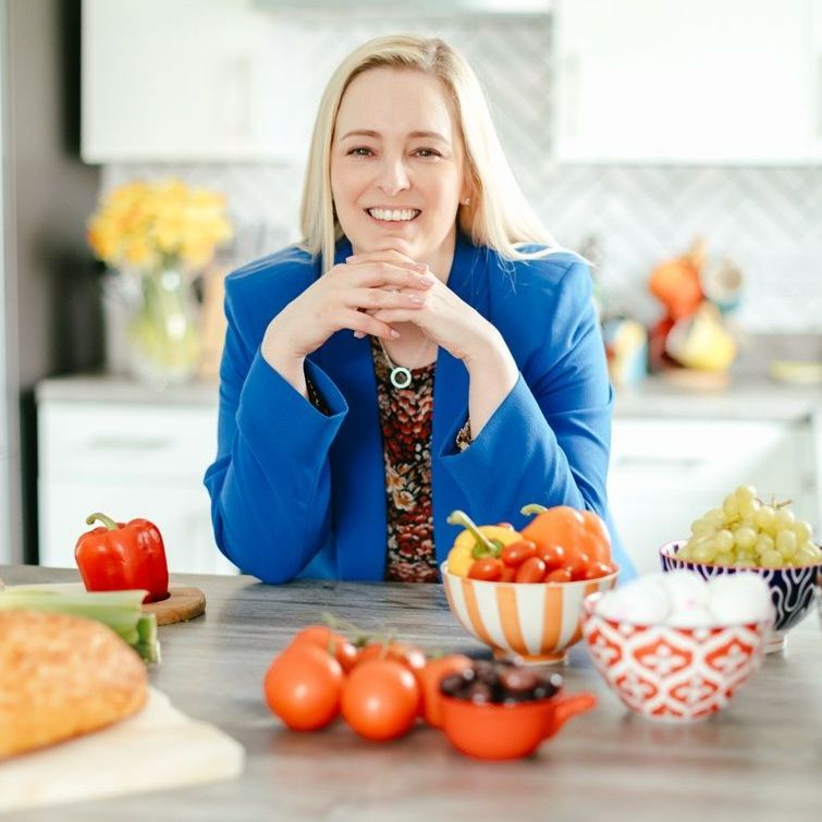 A woman in a blue jacket sits at a table with bowls of fruit and vegetables