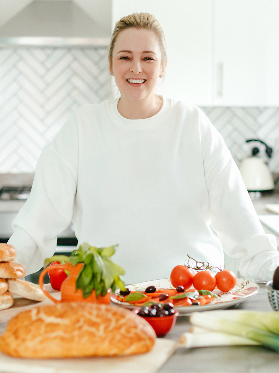 A woman in a white sweater is standing in front of a table full of food.
