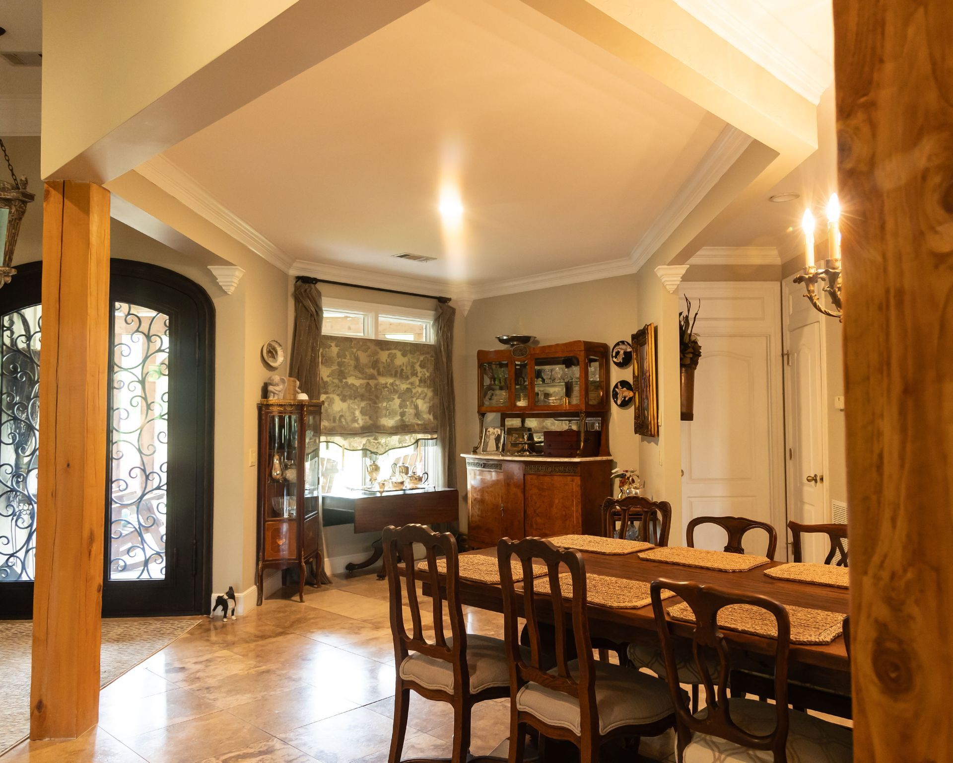 Warm dining room with wooden table and chairs, tall windows, and a china cabinet under vaulted ceilings