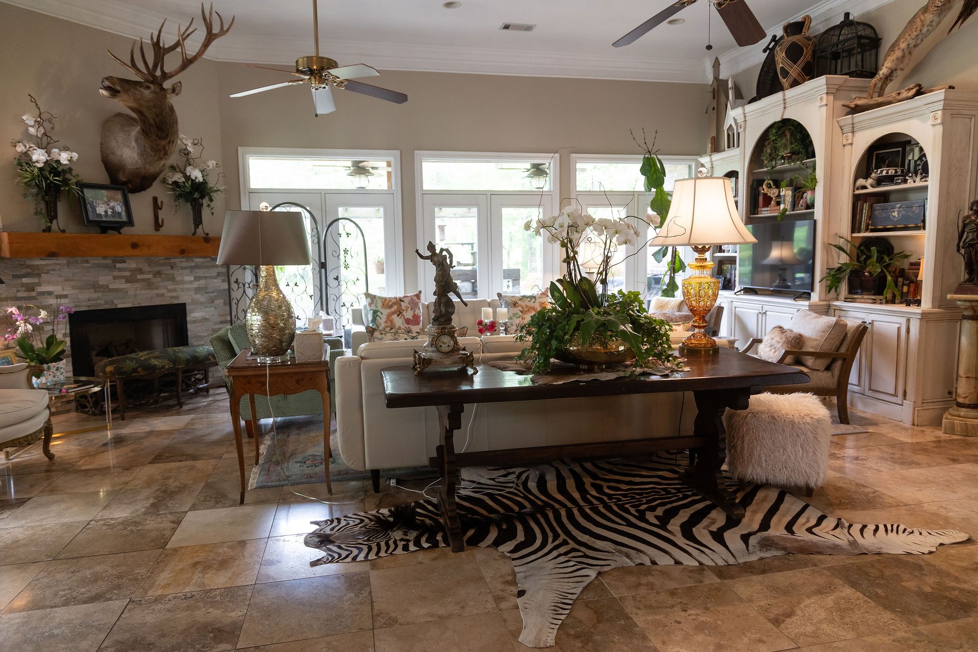 Elegant living room with fireplace, large windows, central table, and zebra rug, decorated with plants and lights