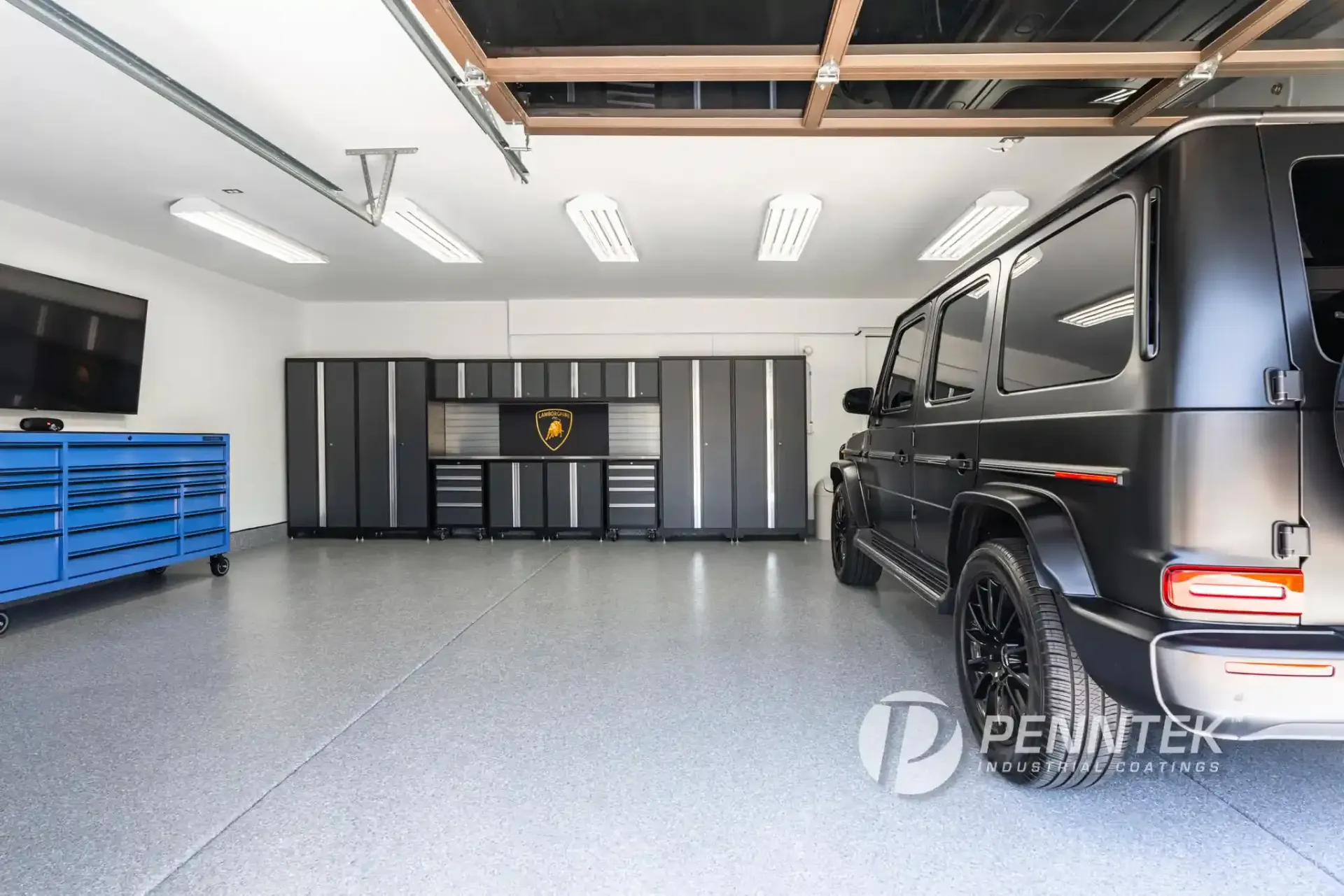 Modern garage interior with gray cabinets, blue tool chest, and a black van parked on the right