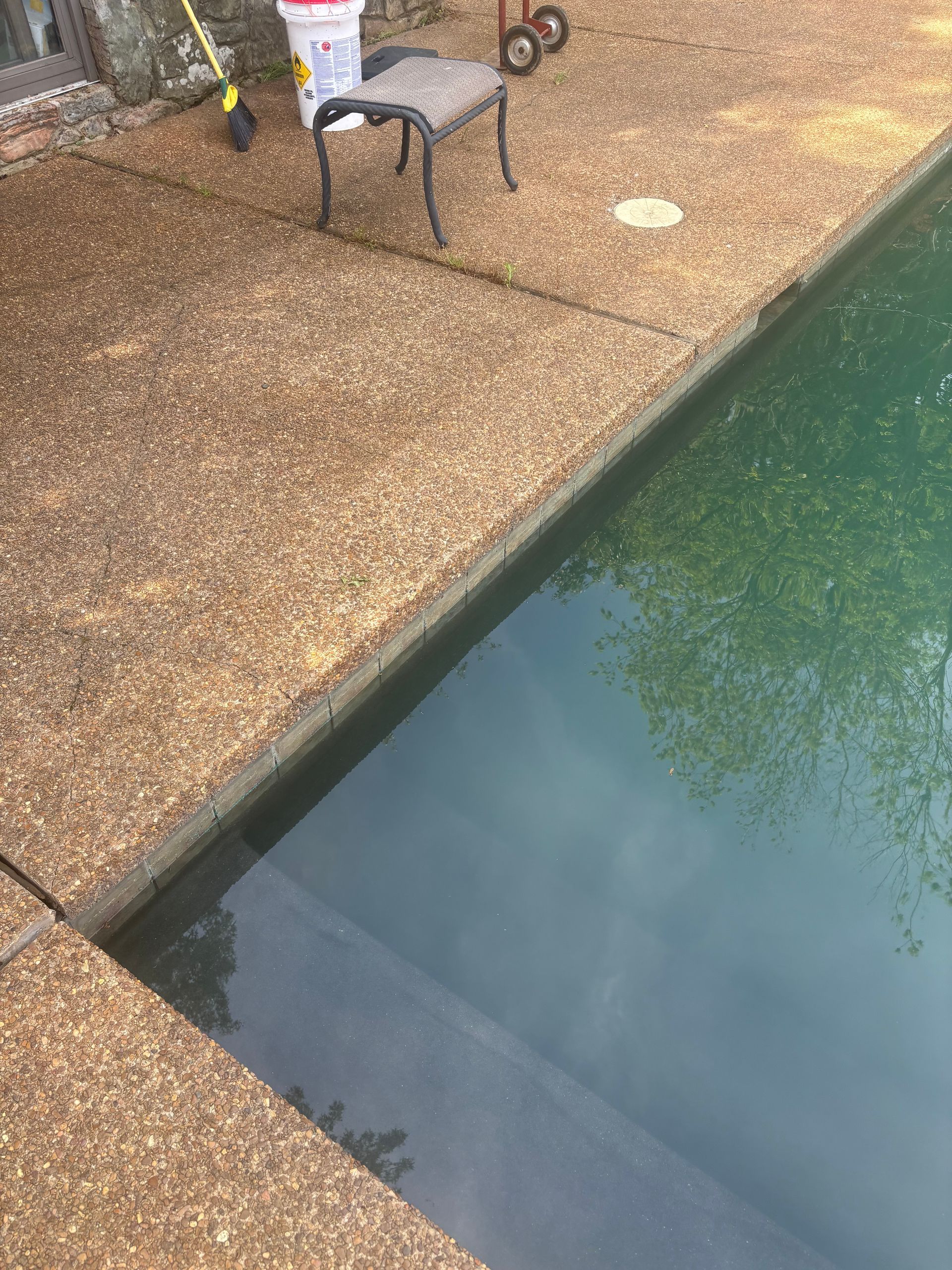 Poolside patio with a small table and chairs beside blue-green pool water