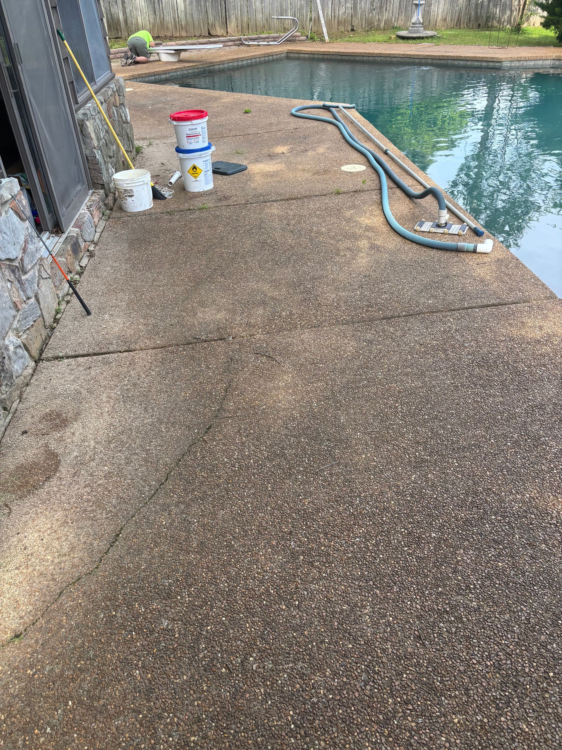 Poolside concrete deck with hose and cleaning supplies beside a pool