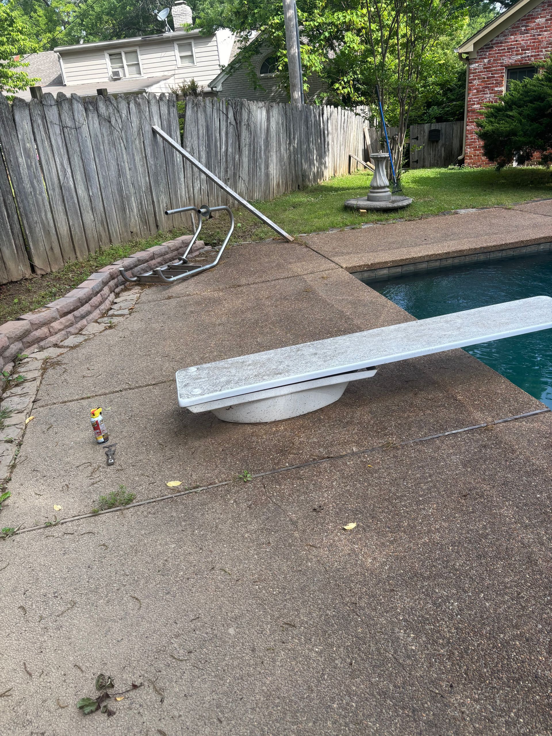 Backyard pool with a diving board beside a small landscaped water feature and fence.