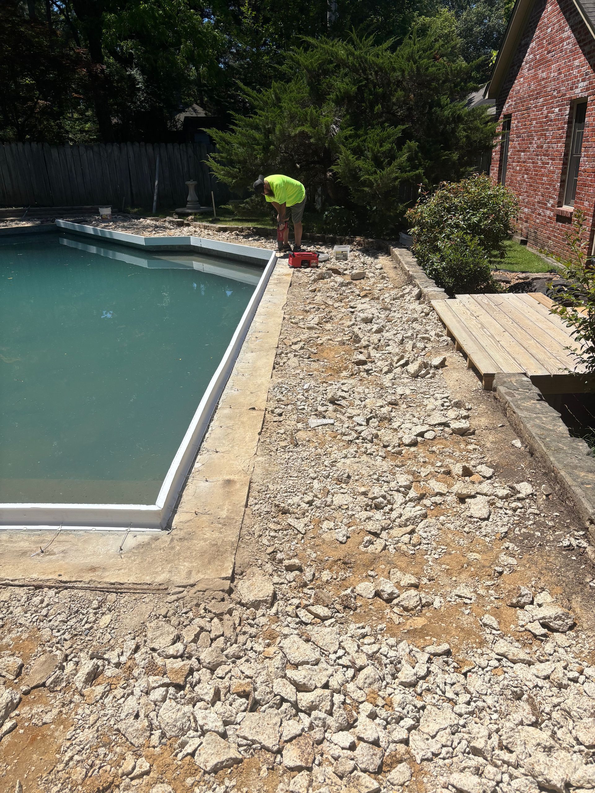 Worker on gravel path beside pool and brick house in sunny backyard