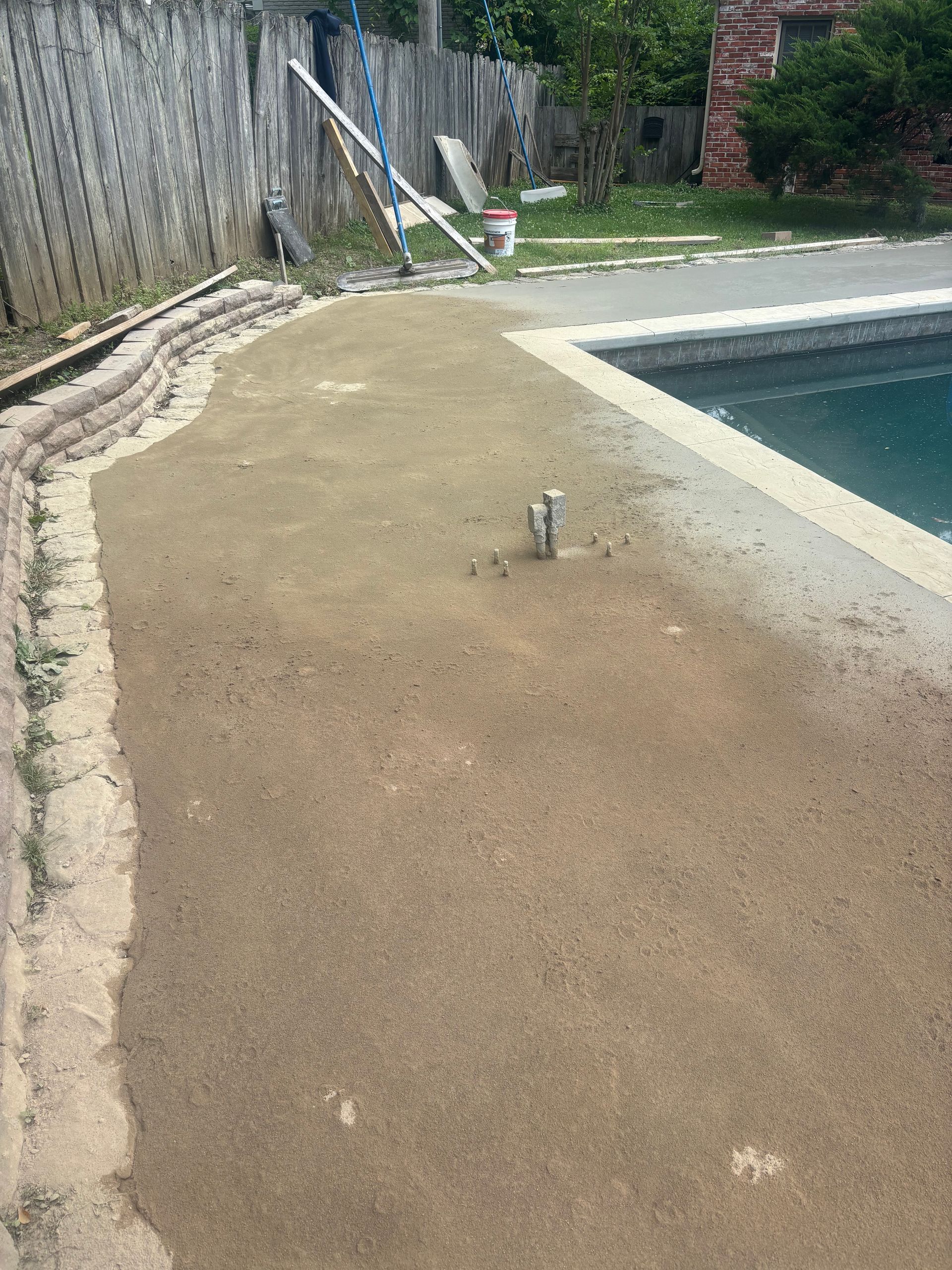 Backyard pool deck with textured concrete, a pool edge, fence, and a lounge chair in the background