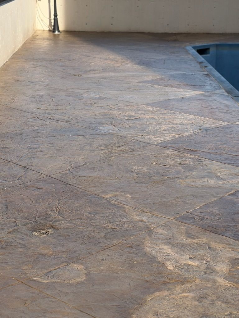 Stone patio beside a swimming pool, with a white wall and sunlight casting shadows.