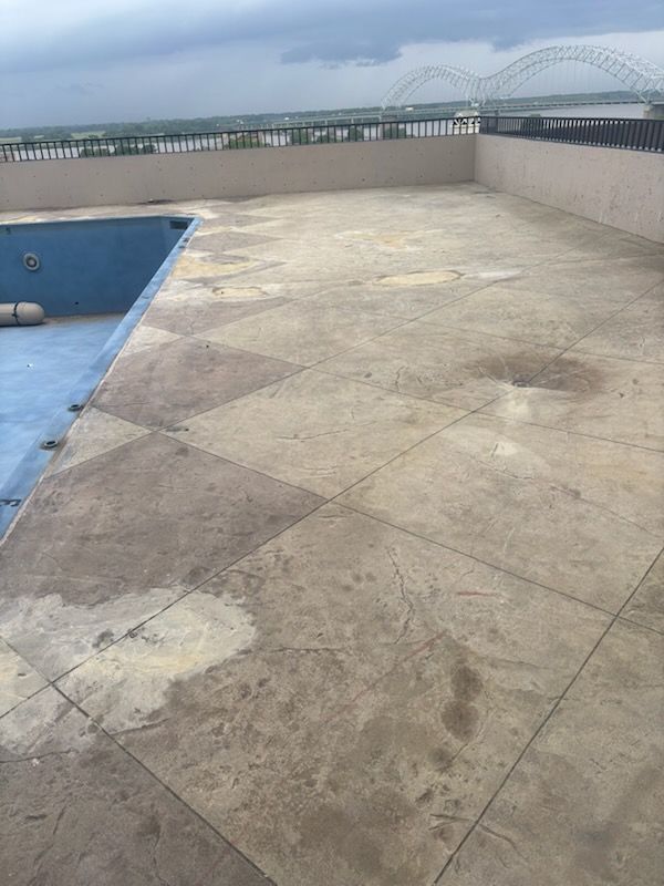 Rooftop terrace with a blue pool edge, wet concrete floor, and a bridge in the distance